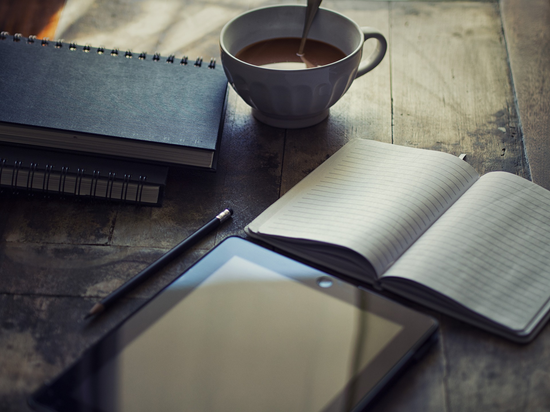 Offenes Notizbuch, Tablet und eine Tasse auf einem dunklen Holztisch